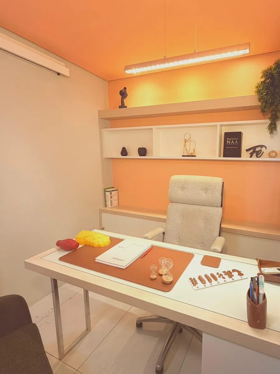 Consultório premium: mesa ampla, cadeira estofada, nichos decorados e parede em tom de laranja