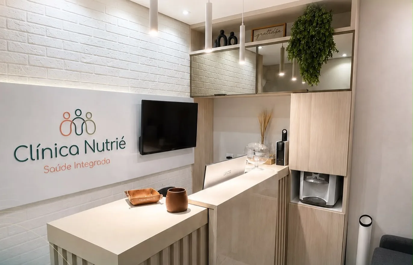 Recepção da Clínica Nutrié, com balcão de madeira clara e a logomarca na parede